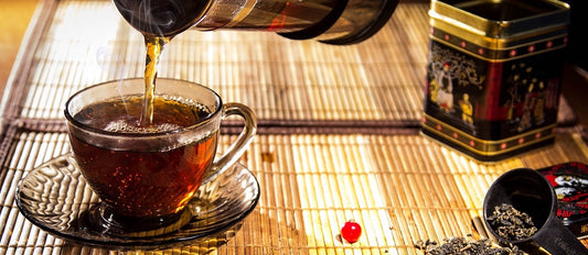 A cup of loose leaf green tea being poured from a french press.