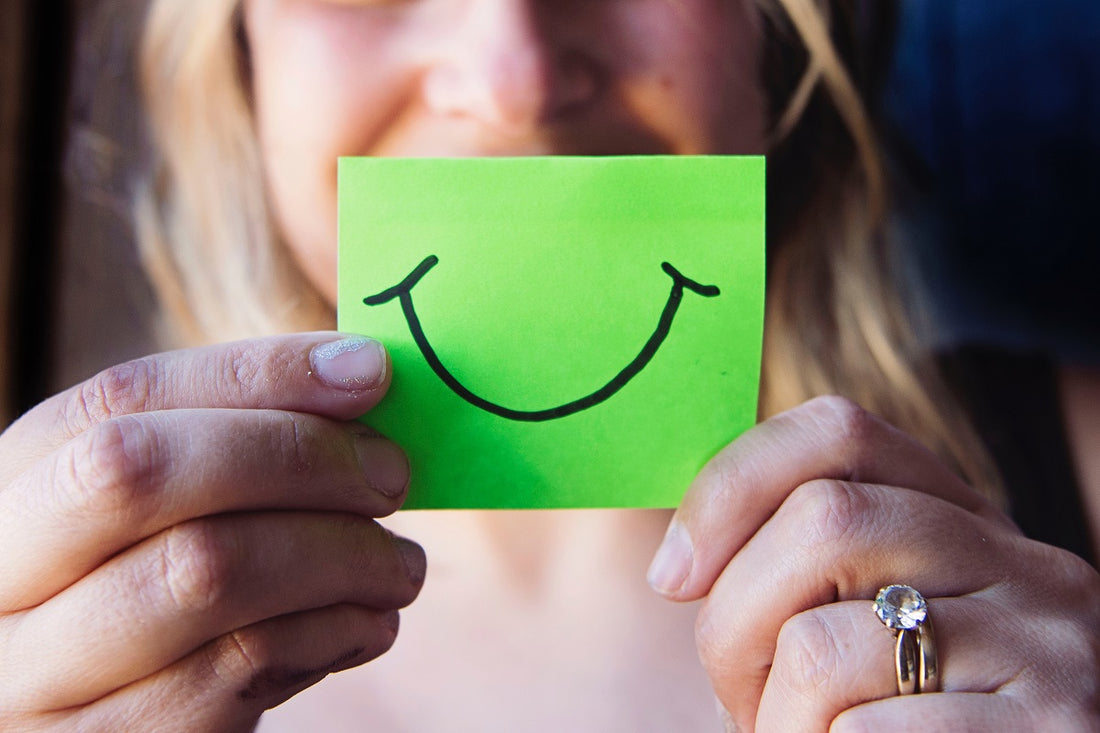 Person holding a post-it note with a smile drawn on it in front of their face.