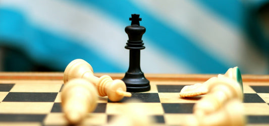 A chessboard with only the black king standing, surrounded by white pieces lying down.