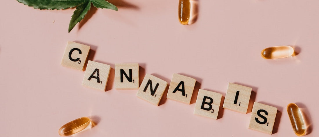 Scrabble tiles spelling out "cannabis" beside filled gel capsules and a marijuana leaf.