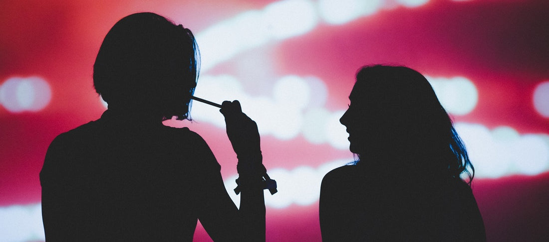 Two people in silhouette standing outside vaping.