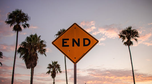 A road sign reading "END" with sky, clouds, and palm trees in the background.