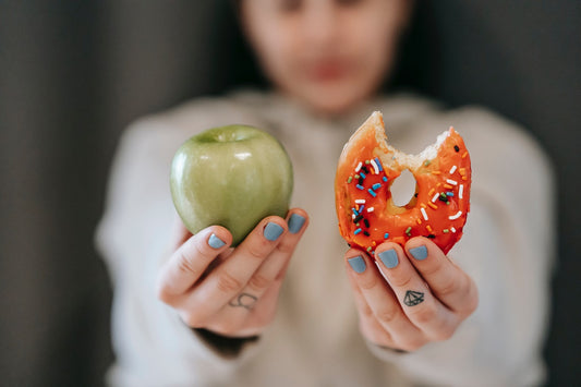 Person holding an apple in one hand, a donut in the other.