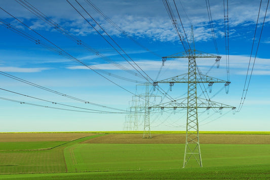 Power lines crossing a green field in front of a bright blue sky.